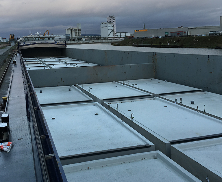Precast concrete parts from ZAPF safely stacked in the hold of a barge under cloudy skies.