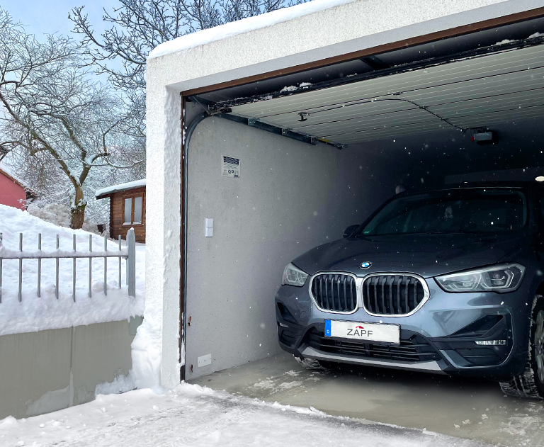 BMW X1 standing in an open ZAPF garage with snow and a wintry landscape in the background.