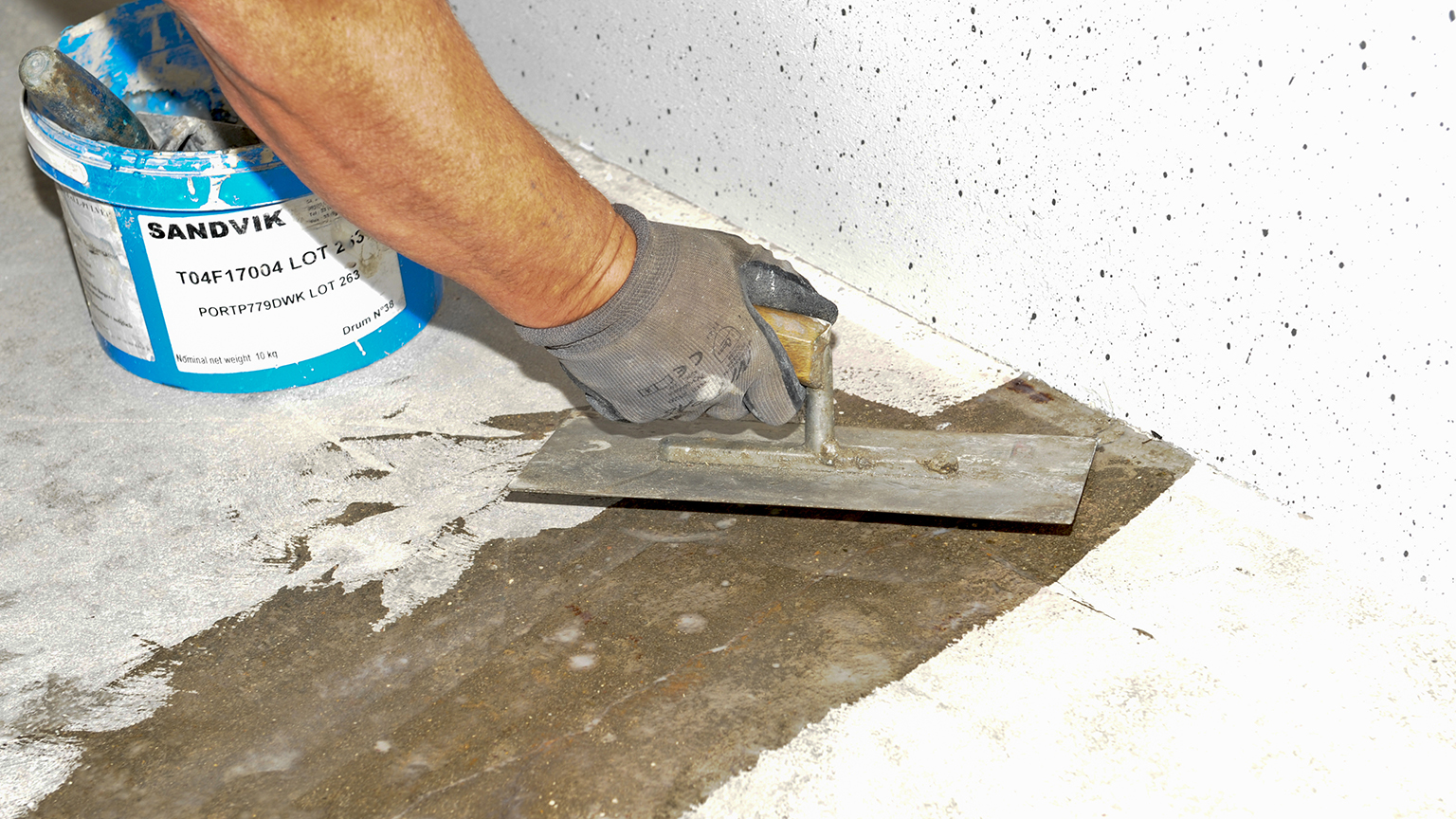 Handwerker trägt mit einer Kelle Mörtel auf einen Garagenboden auf.