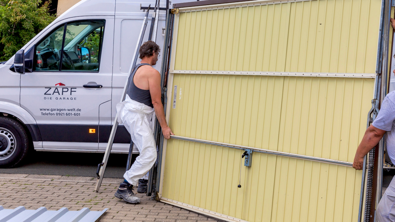 zapf_blog_beitragstitel_alttor Zwei Handwerker demontieren ein gelbes Garagentor vor einem Servicefahrzeug.