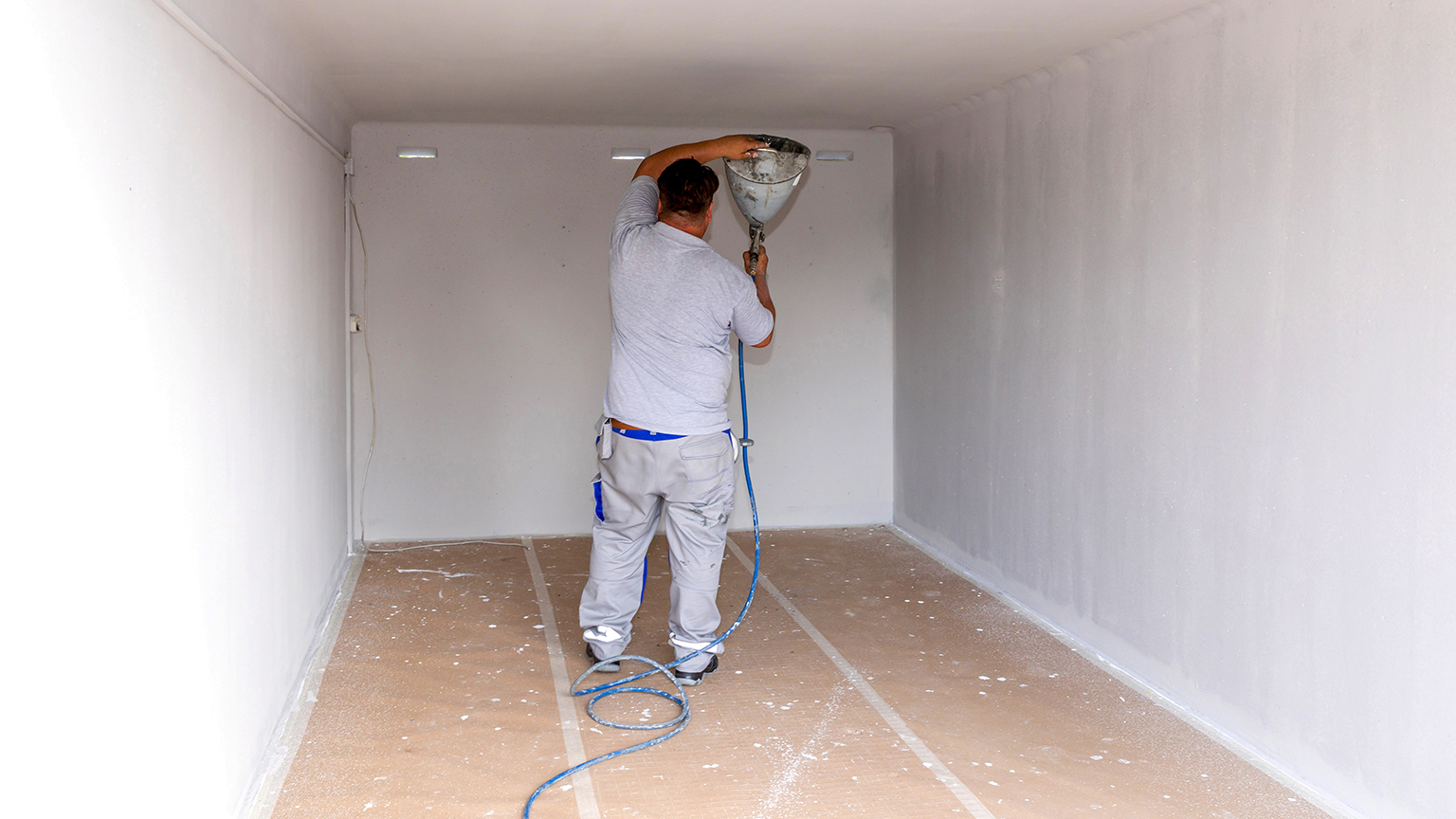 zapf_blog_beitragstitel_arbeiten Handwerker sprüht weiße Farbe mit Spritzpistole an die Wand einer Garage.