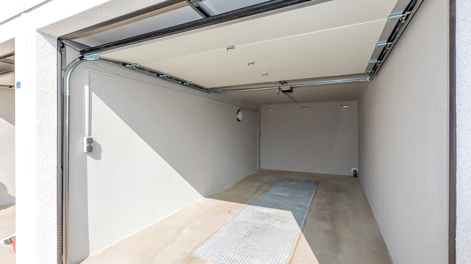 zapf_blog_beitragstitel_augen_auf Leere Einzelgarage mit offenem Sektionaltor und Betonboden.