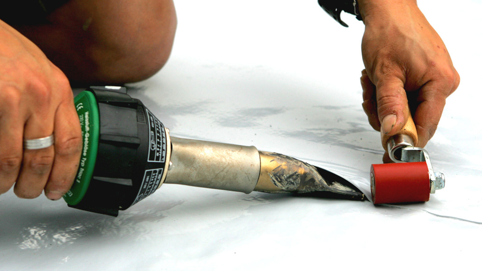 Handwerker verschweißt Dachfolie mit Heißluftfön und Andrückrolle.