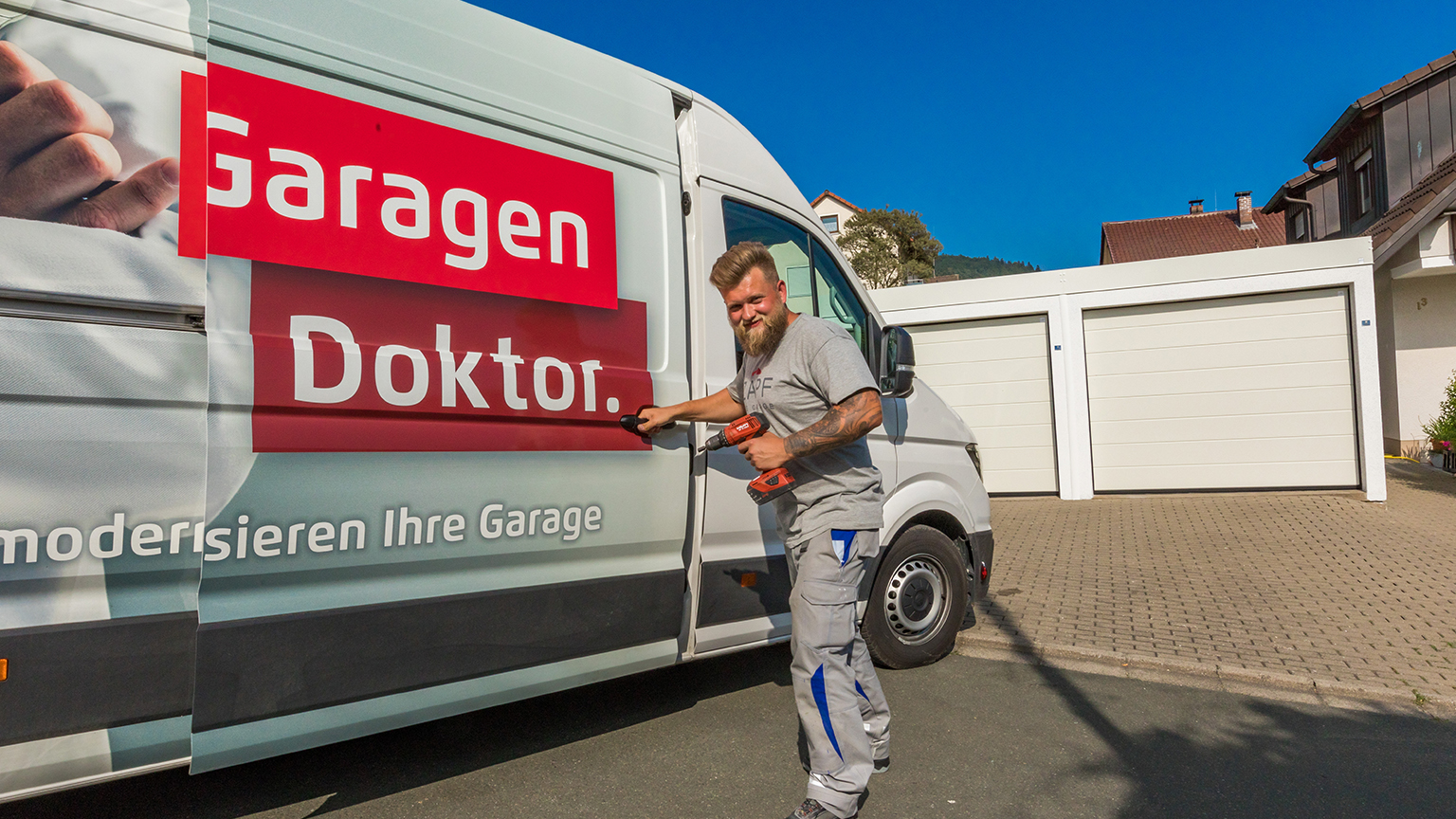 Handwerker mit Akkuschrauber öffnet Tür eines Servicewagens mit Aufschrift „Garagen Doktor“.