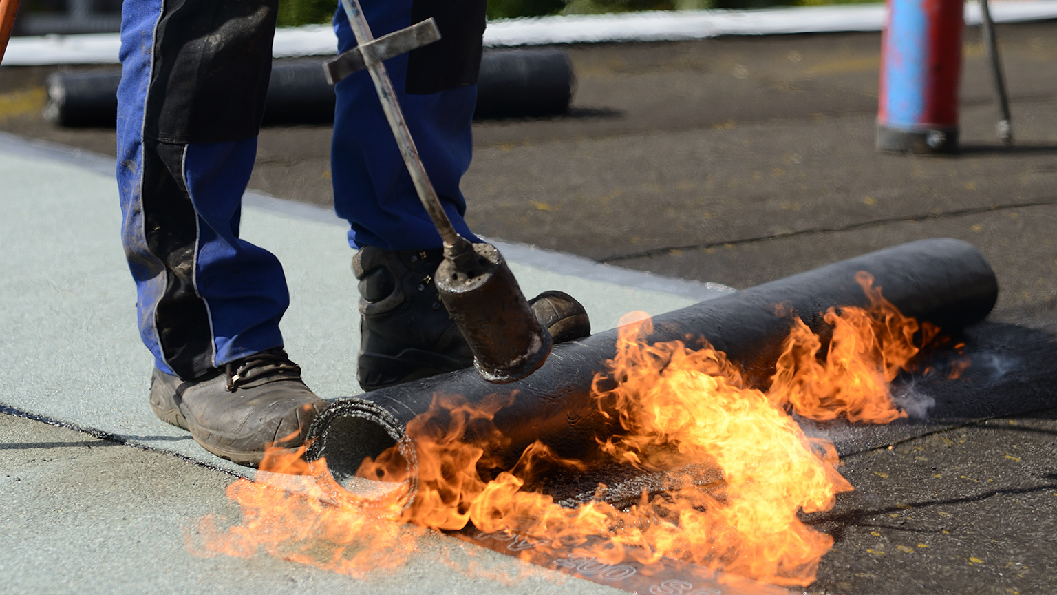 Handwerker verschweißt Dachpappe mit offener Flamme auf Flachdach.