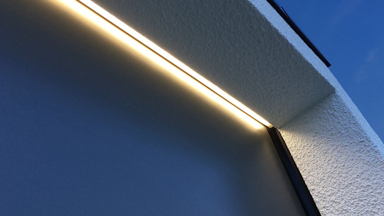 zapf_blog_beitragstitel_dunkel Nahaufnahme einer warmweißen LED-Lichtleiste über Garagentorrahmen bei Abendhimmel.