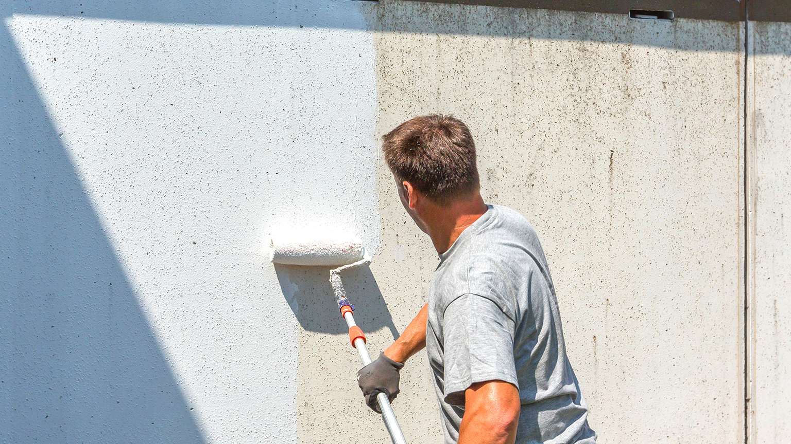 Handwerker streicht verschmutzte Garagenwand mit weißer Farbe.