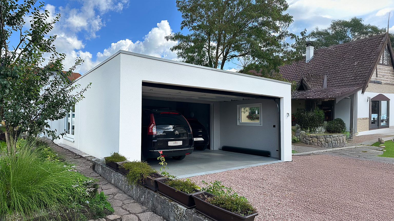 Auto in einer Doppelgarage mit geöffnetem Tor in einem. Wohngebiet vor blauem Himmel.