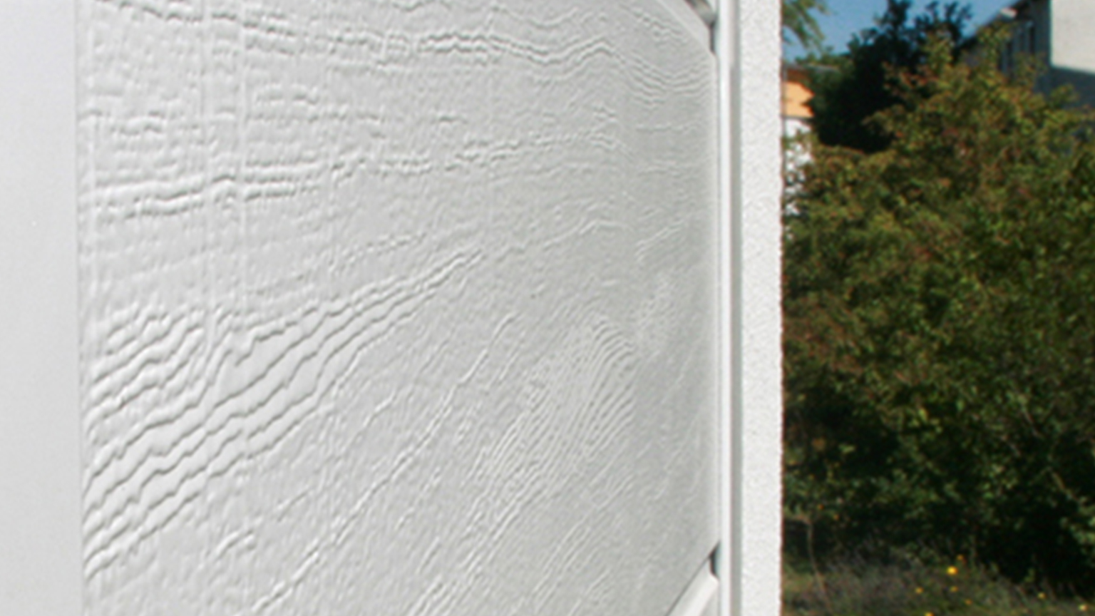 zapf_blog_beitragstitel_garagenoeffner Nahaufnahme einer weißen Garagenwand mit sichtbarer Holzmaserung.