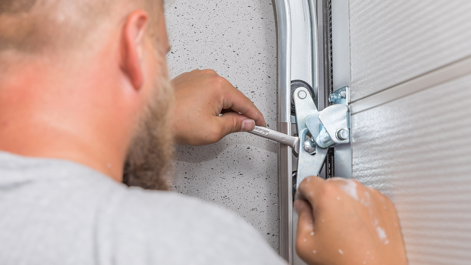 Handwerker zieht mit Maulschlüssel Schraube an Garagentormechanismus fest.