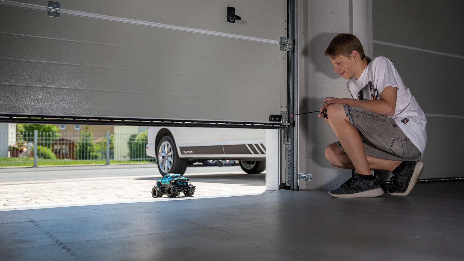 Junge steuert ferngesteuertes Auto unter halb geöffnetem Garagentor hindurch.