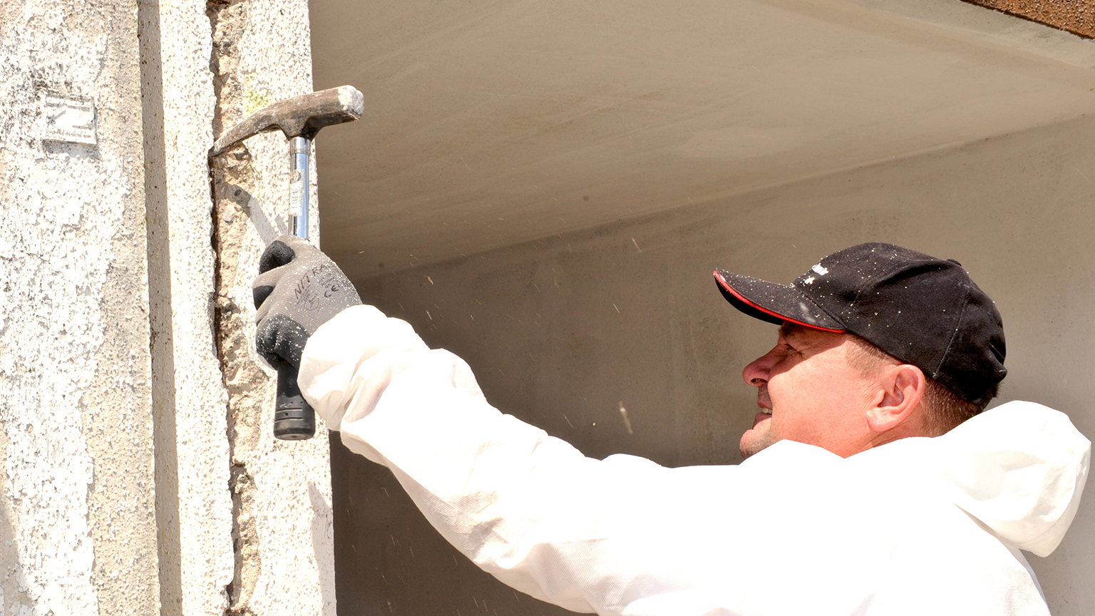 Handwerker entfernt mit Hammer und Meißel beschädigten Beton an Garagenecke.