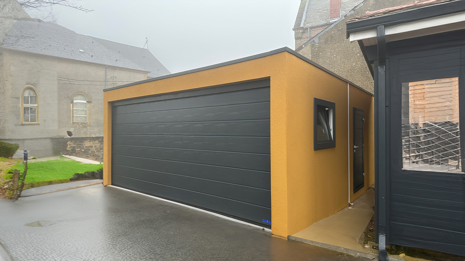 Moderne Großraumgarage mit gelber Fassade und schwarzem Sektionaltor an einem nebligen Tag.