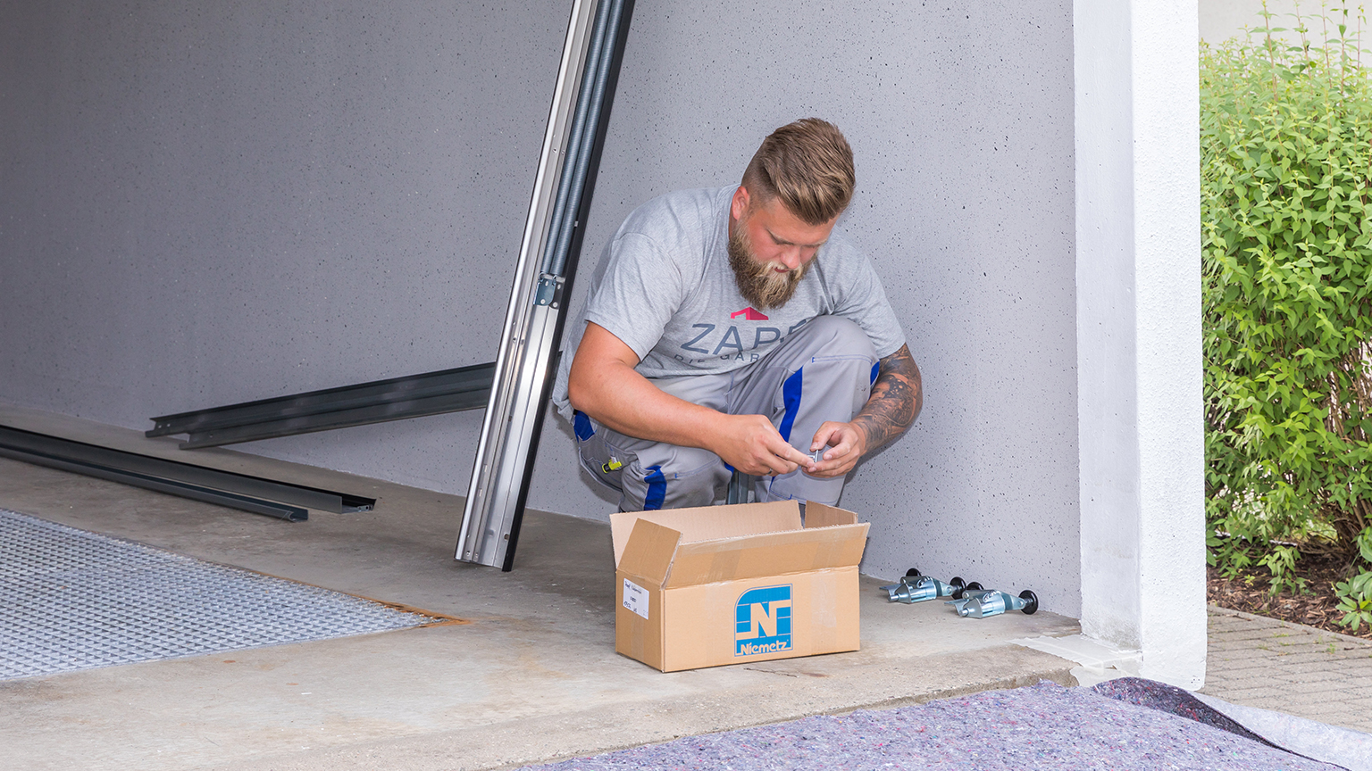zapf_blog_beitragstitel_hubtor Monteur kniet vor Garage und sortiert Kleinteile aus einem Karton.