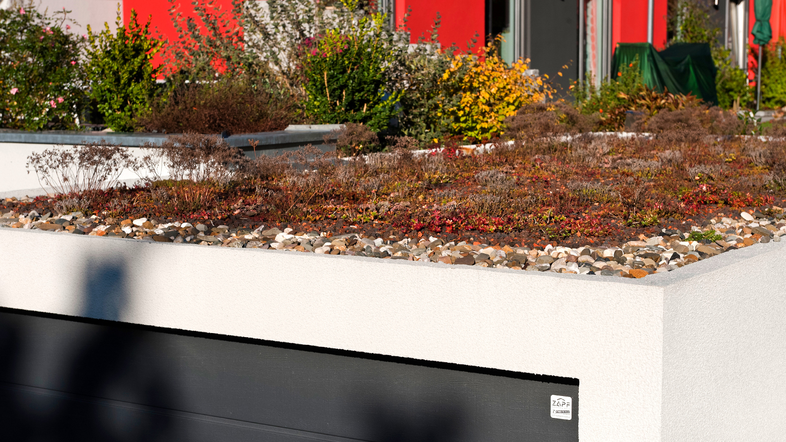 Garage mit extensiv begrüntem Dach und umlaufendem Kiesrand im Herbst.