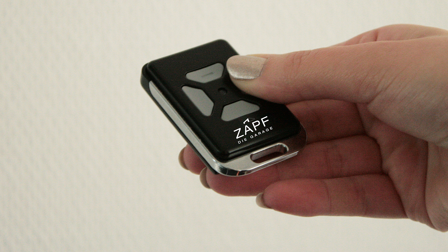 zapf_blog_beitragstitel_komfort Hand hält schwarzen ZAPF Garagentoröffner vor hellem Hintergrund.