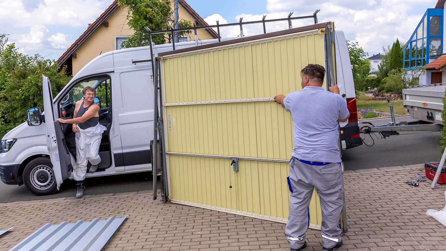 Handwerker steigt aus einem Transporter zu einem Handerwerker der ein Garagentor hält.