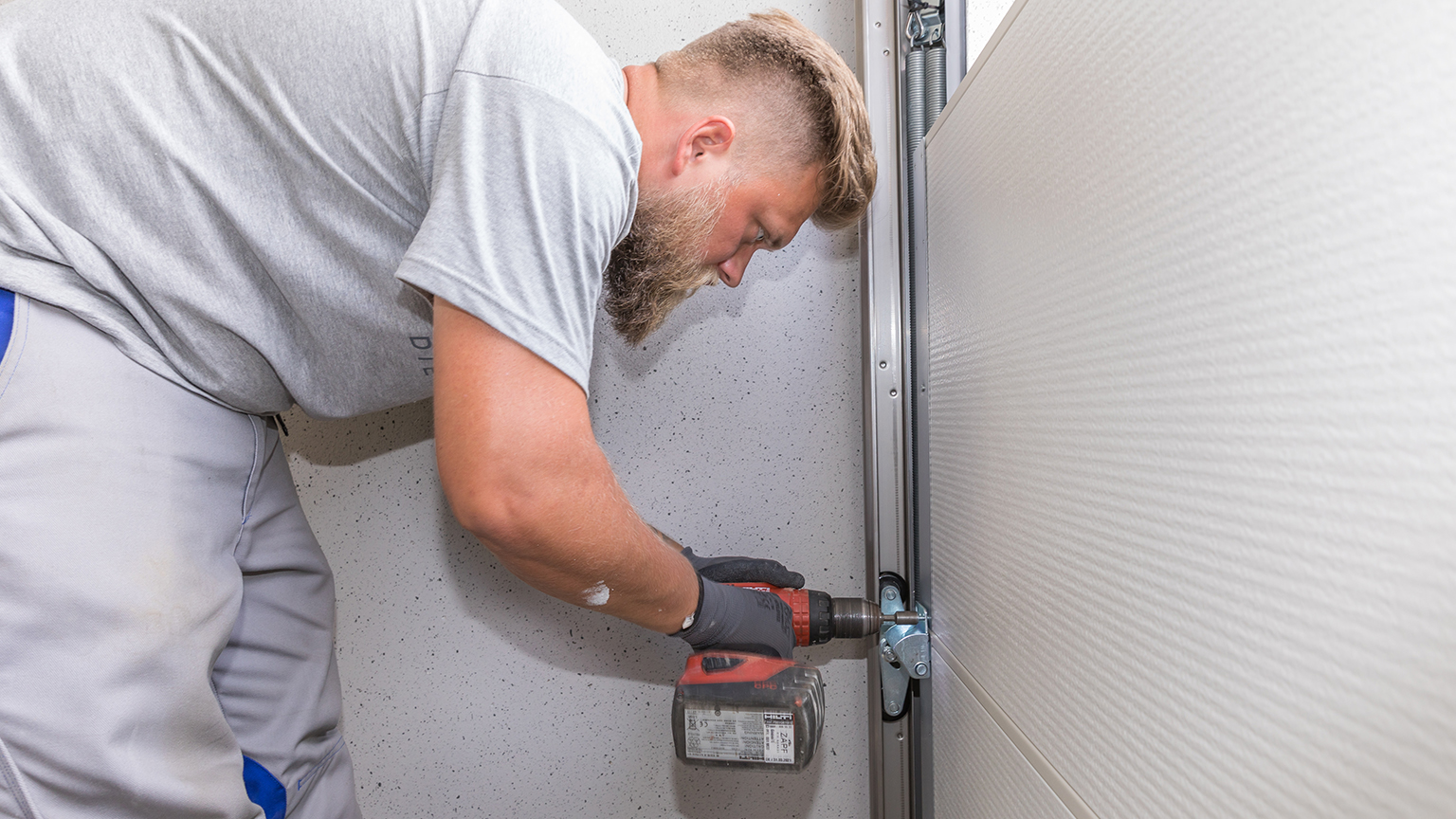 zapf_blog_beitragstitel_luxus Handwerker befestigt mit Akkuschrauber Beschlag am Garagentor.
