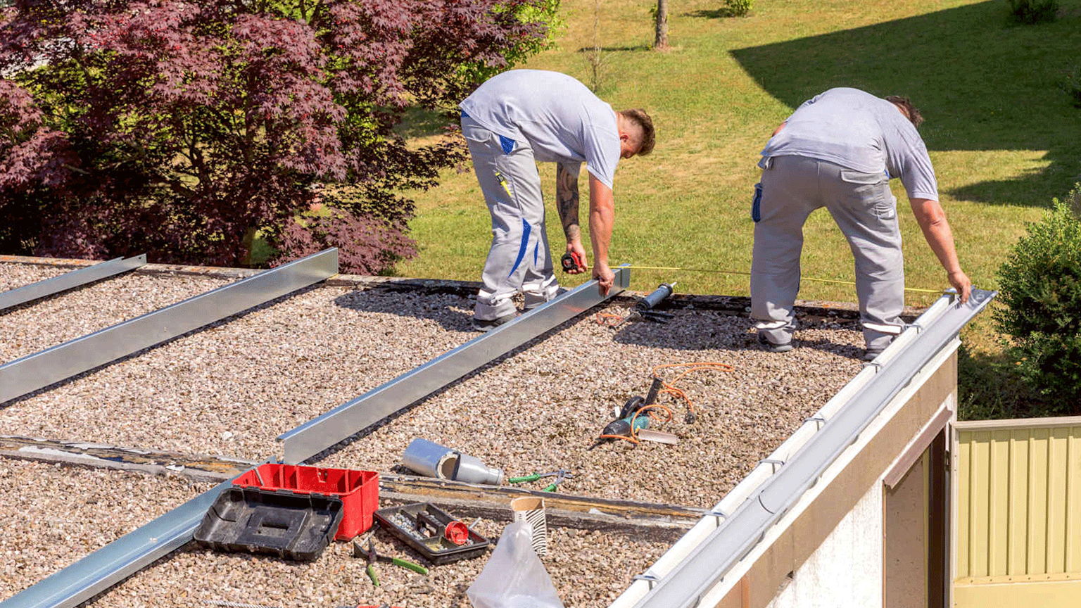 Zwei Handwerker montieren Metallprofile auf einem Kies-Flachdach.