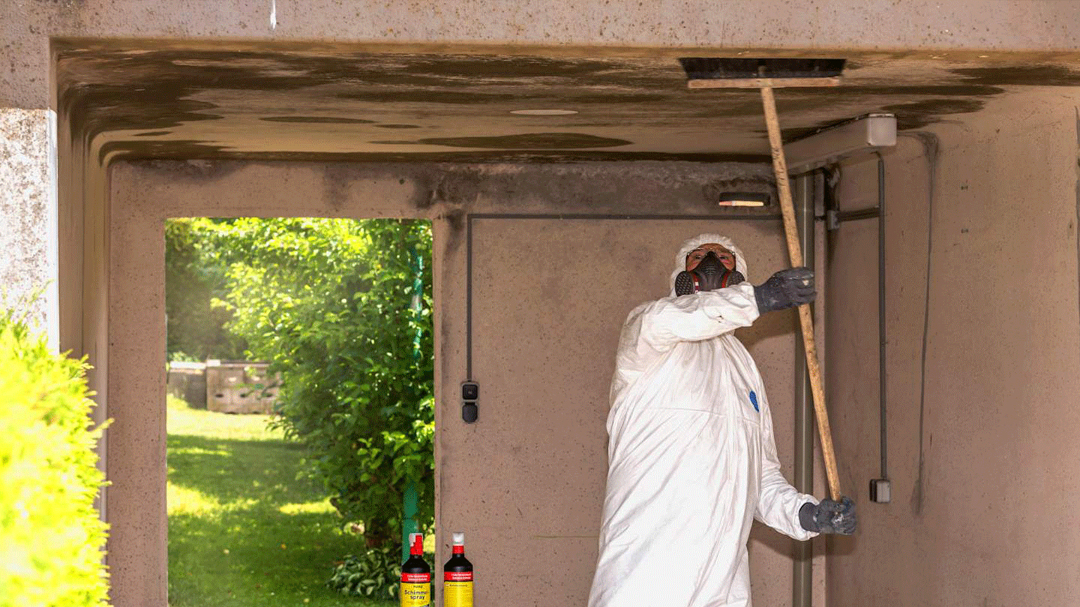 Arbeiter in Schutzanzug entfernt Schimmel von einer Garagendecke.