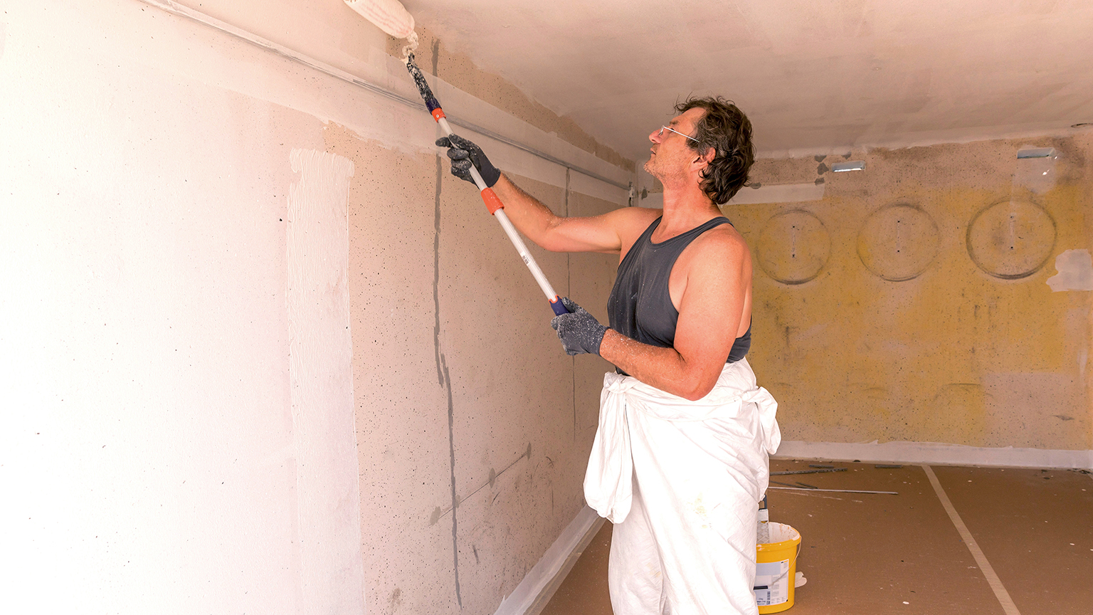 zapf_blog_beitragstitel_neubau Handwerker streicht Garagendecke mit weißer Farbe und Farbrolle an Teleskopstiel.