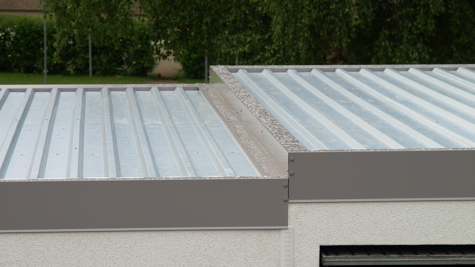 Nahaufnahme eines Flachdachs mit grauem Trapezblech und Attika-Abdeckung.