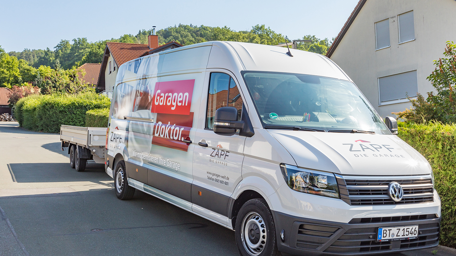 zapf_blog_beitragstitel_renovierung Firmenfahrzeug mit der Aufschrift „Garagen Doktor“ und Anhänger in einer Wohnstraße.