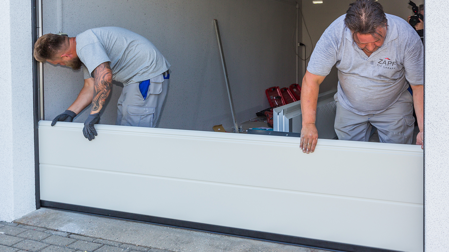 zapf_blog_beitragstitel_renovierung Zwei Monteure setzen ein weißes Garagentor-Sektionsteil in die Führungsschienen ein.