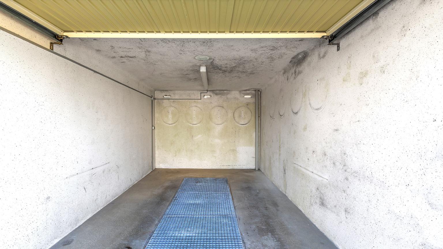 zapf_blog_beitragstitel_rost Innenansicht einer Garage mit verschmutzten und fleckigen Wänden sowie offenem Garagentor.