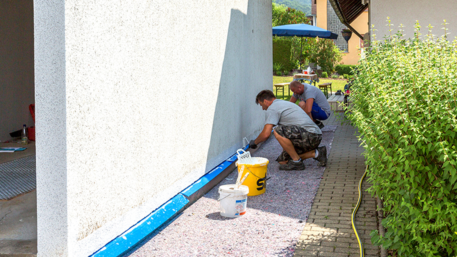 Zwei Handwerker sanieren die Außenwand einer Fertiggarage und tragen neuen Putz auf