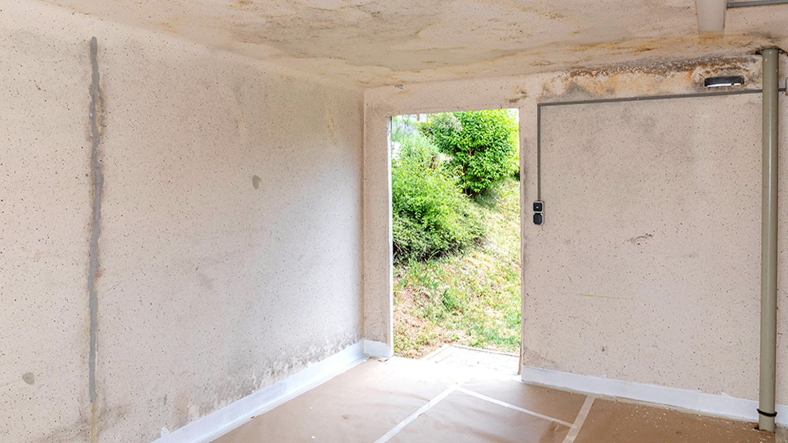 Innenansicht einer sanierungsbedürftigen Fertiggarage mit Feuchtigkeitsspuren an Wänden und Decke