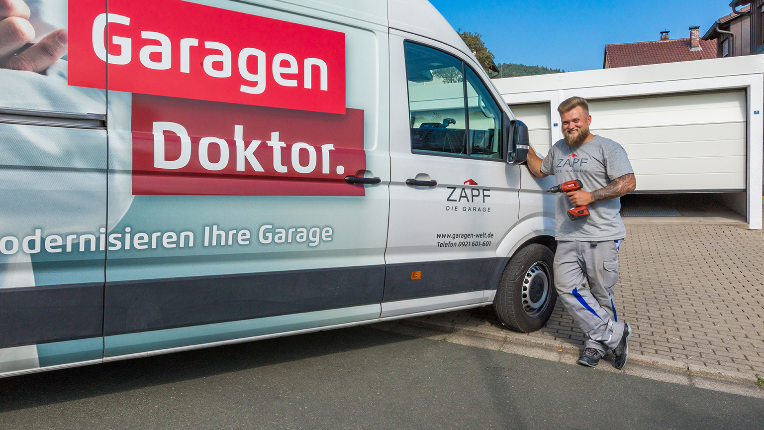 zapf_blog_beitragstitel_sanierung Handwerker lehnt mit Akkuschrauber an Servicefahrzeug mit Aufschrift „Garagen Doktor“.