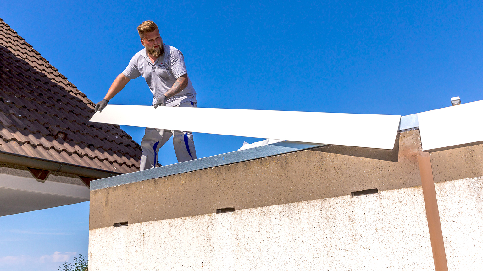 Handwerker hebt lange weiße Abdeckleiste auf Garagendach.