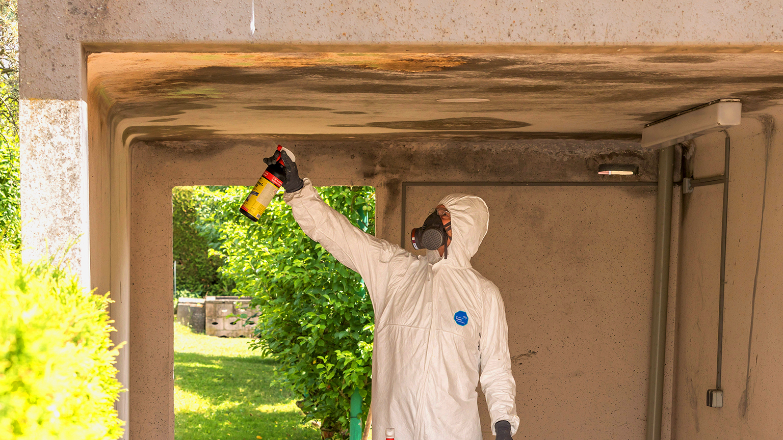 Arbeiter im Schutzanzug sprüht Schimmelentferner an Garagendecke.