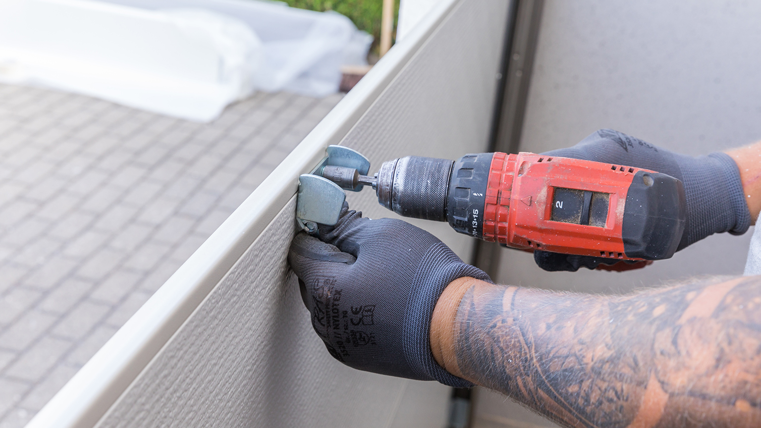 Handwerker befestigt Metallscharnier an Garagentor mit Akkuschrauber.