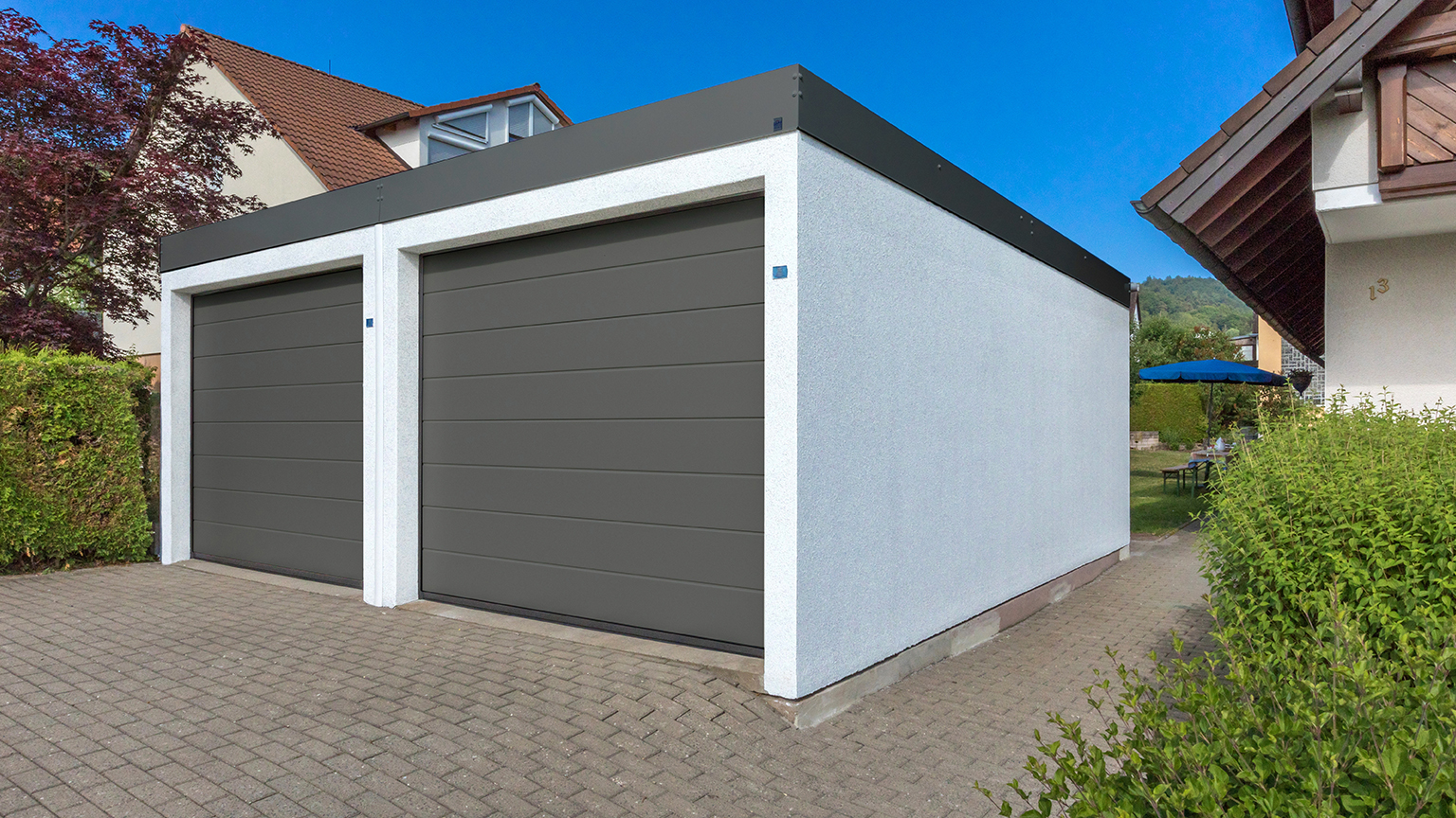 Doppelgarage mit grauen Sektionaltoren und Flachdach.