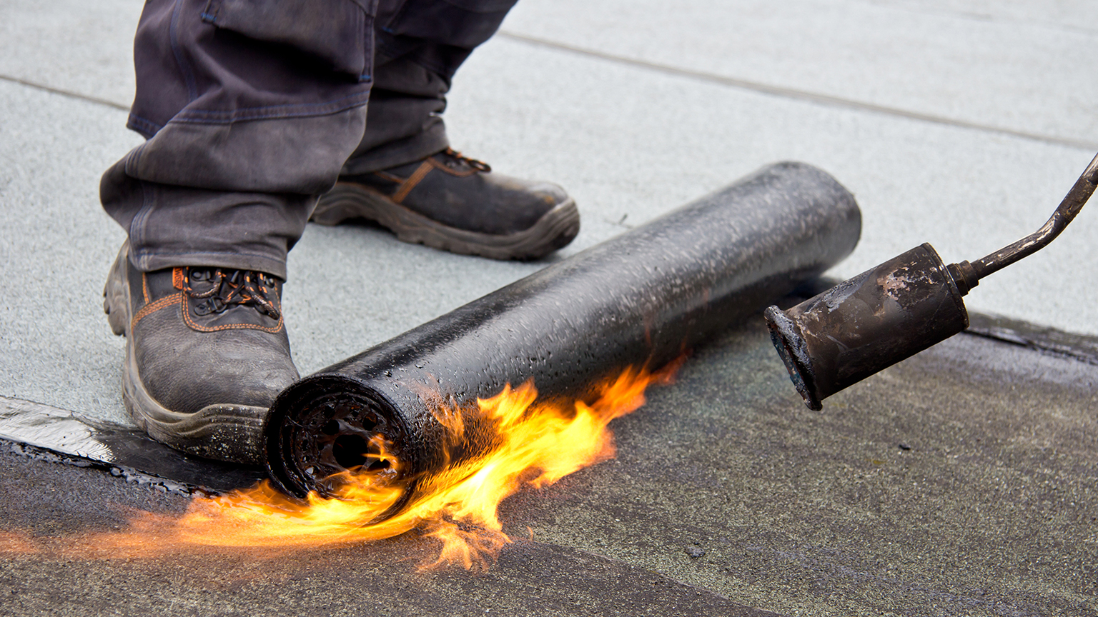 zapf_blog_beitragstitel_top5 Handwerker erhitzt Dachpappe mit Gasbrenner bei der Abdichtung einer Fläche.