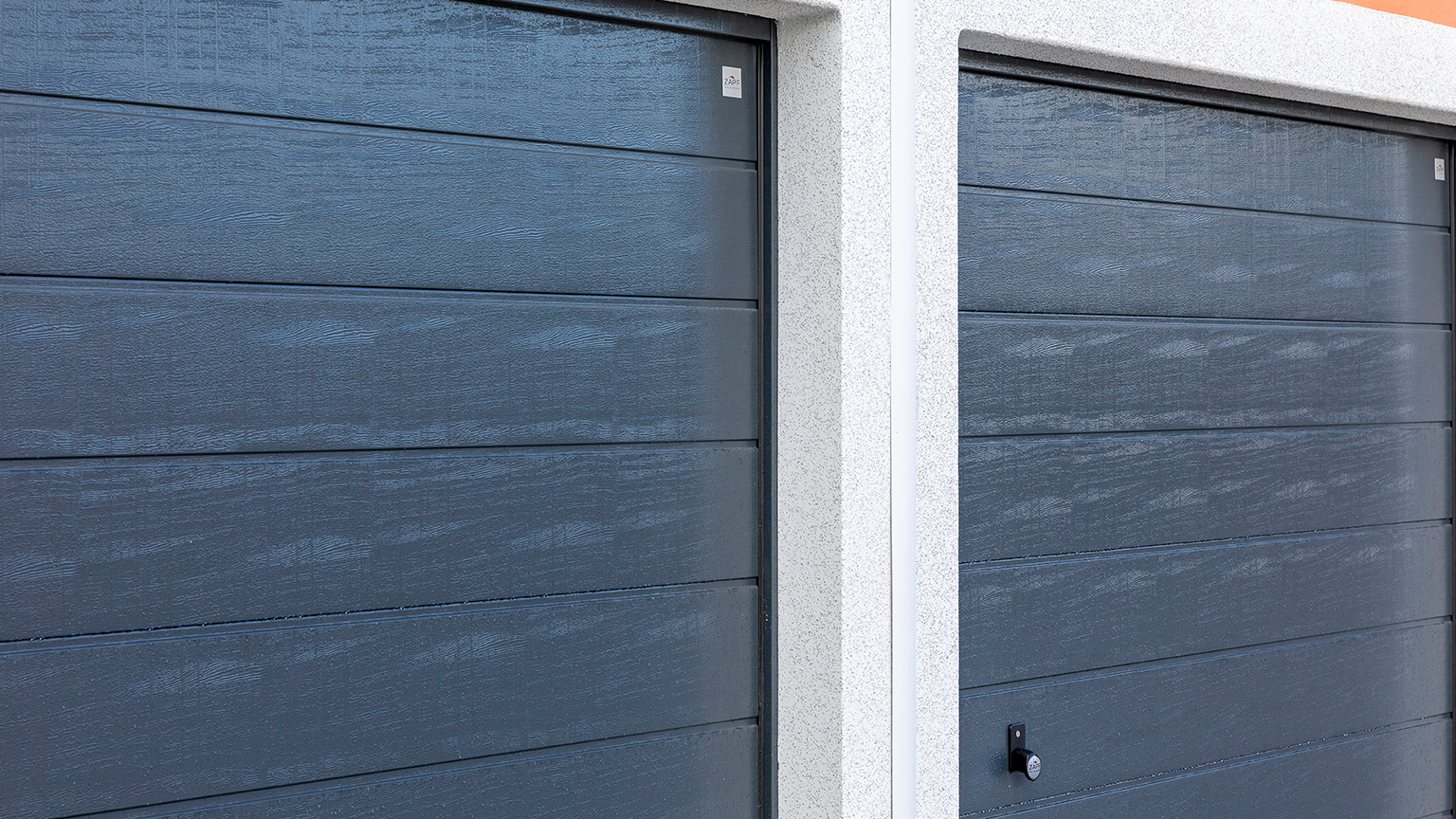 Nahaufnahme zweier nebeneinanderliegender dunkelgrauer Garagentore mit Holzstruktur.