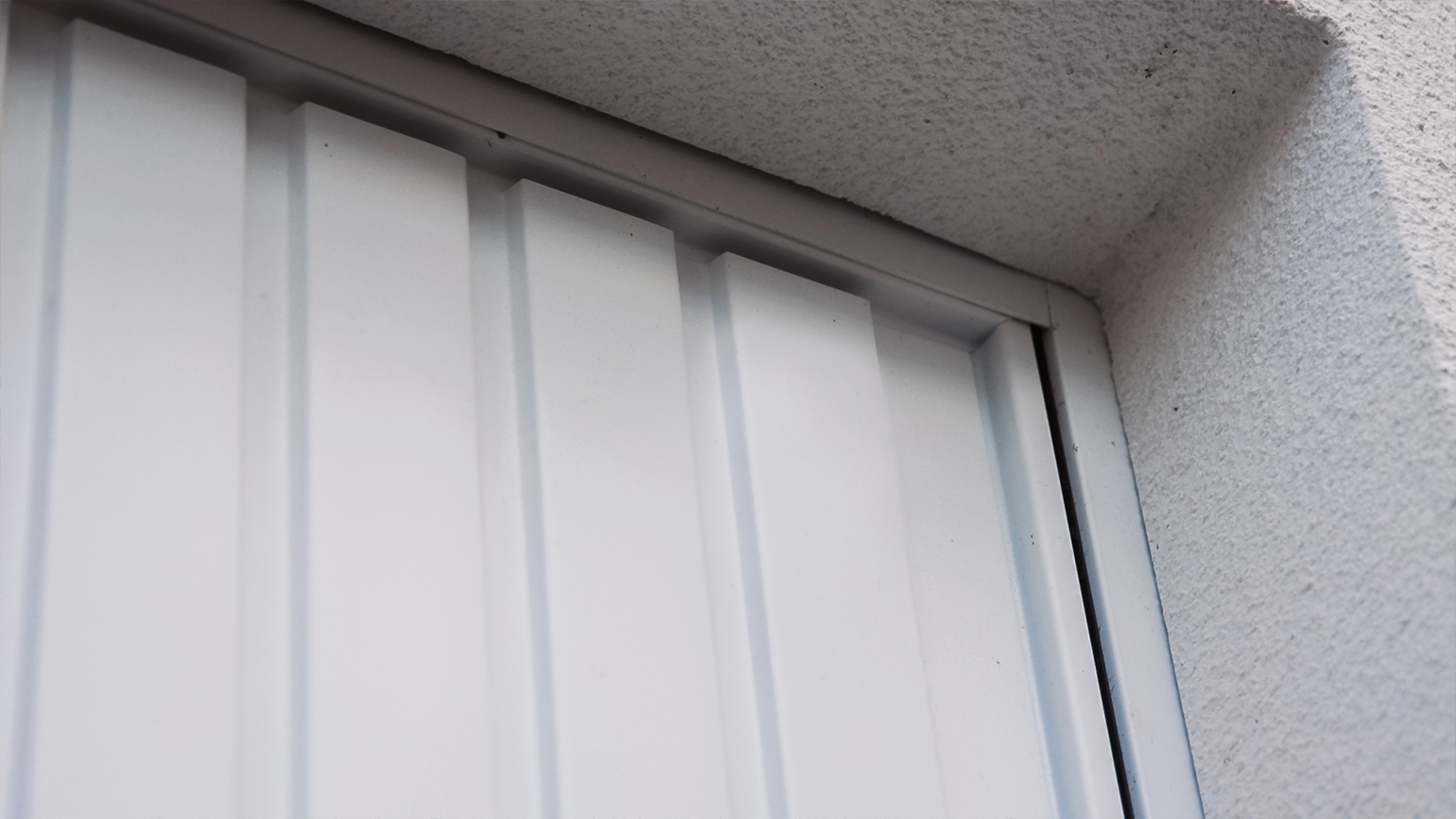 Nahaufnahme eines weißen Garagentors mit senkrechter Sickenstruktur im Rahmen.