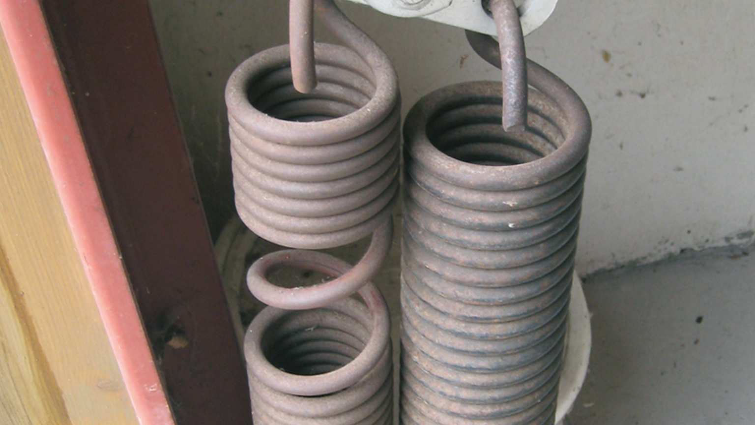 zapf_blog_beitragstitel_torfedern Nahaufnahme von zwei stark beanspruchten Garagentorfedern, eine davon gebrochen.