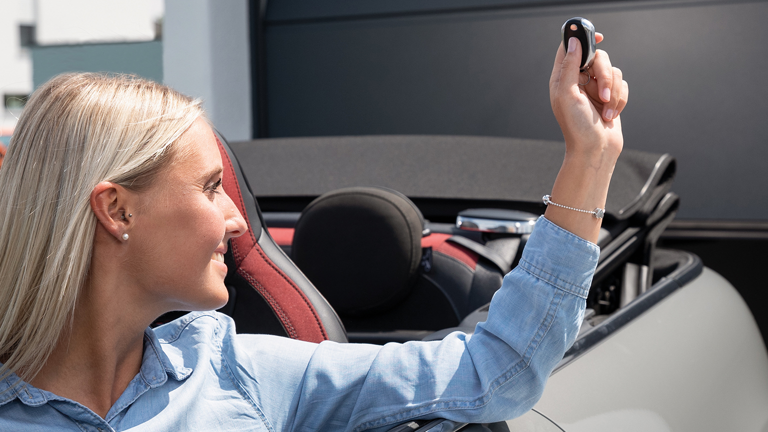 Frau sitzt im Cabrio und hält einen Garagentoröffner nach oben.