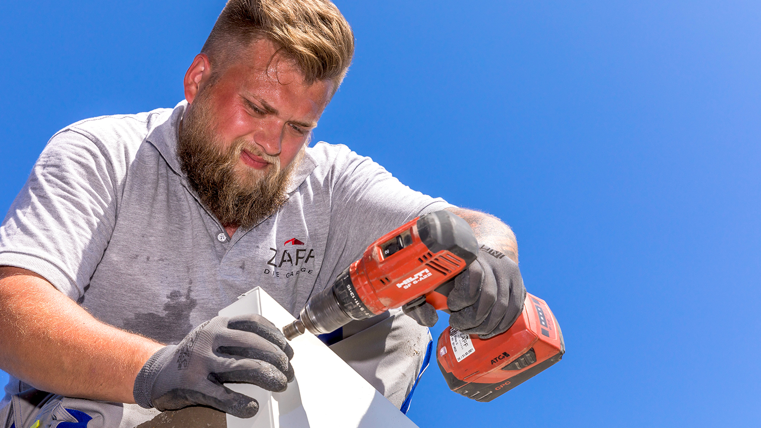 zapf_blog_beitragstitel_wetter Handwerker schraubt mit Akkubohrmaschine an einem Bauteil unter blauem Himmel.