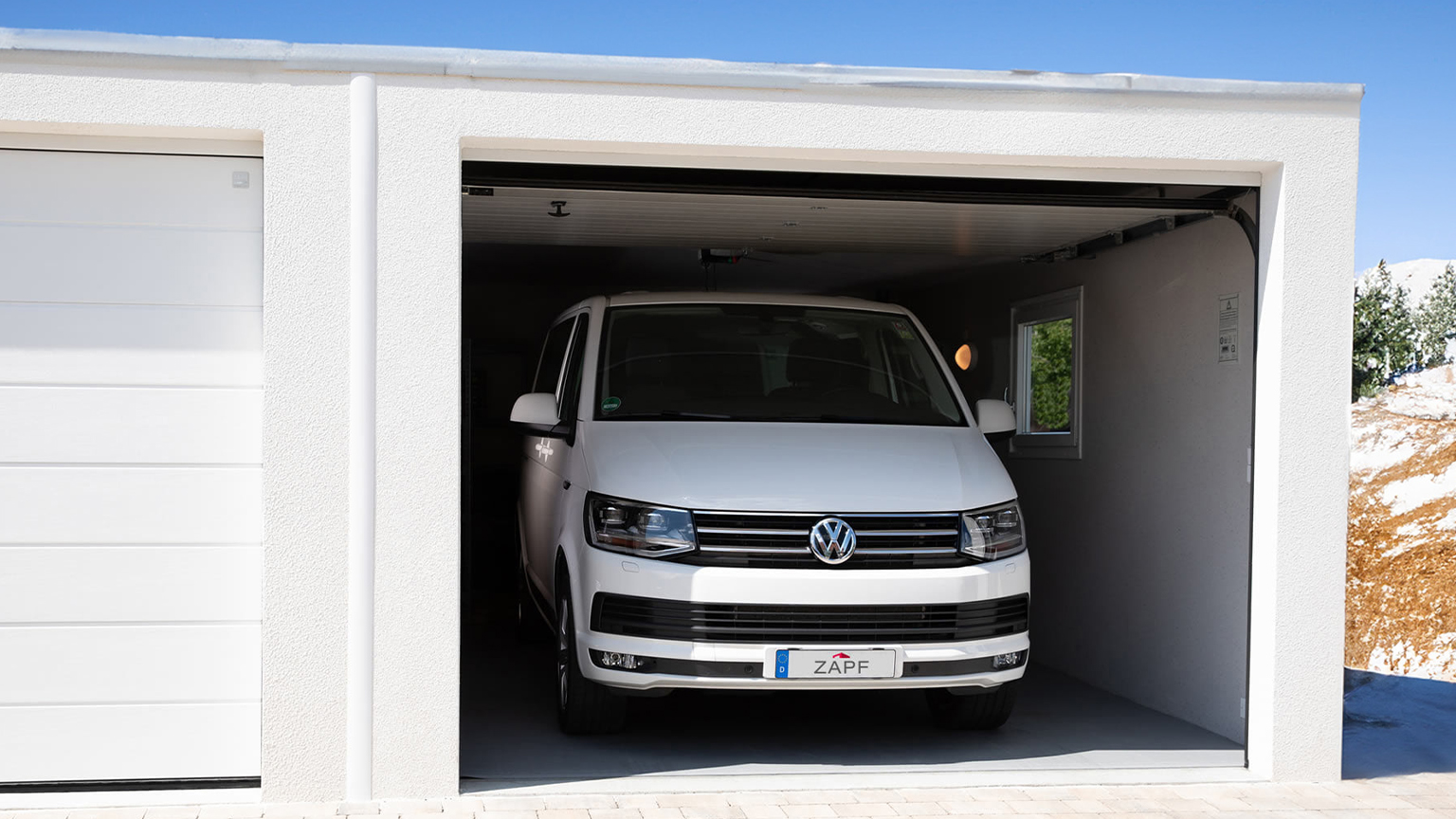zapf_blog_beitragstitel_winter Weißer VW-Bus steht in einer geöffneten Garage mit weißer Fassade.