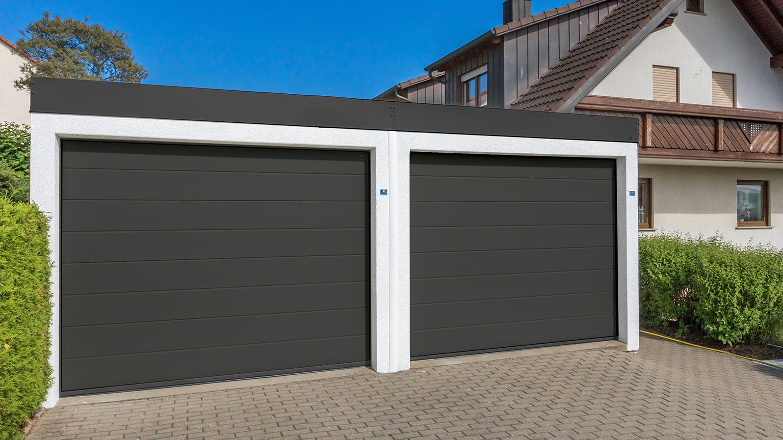 Doppelgarage mit schwarzen Sektionaltoren vor Wohnhaus.