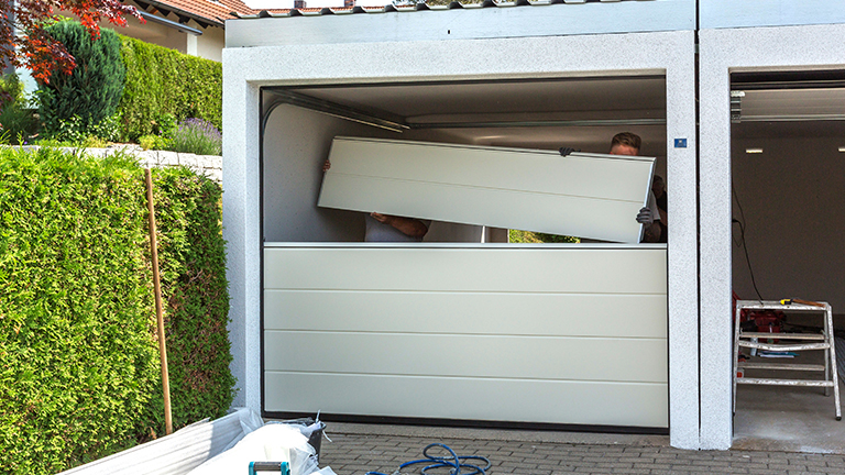 Installation of a new sectional door in a prefabricated garage by two fitters in summer weather