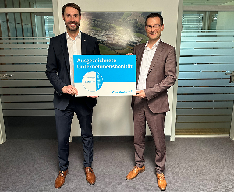 Zwei Männer im Anzug halten eine Auszeichnung von Creditreform für „Ausgezeichnete Unternehmensbonität“ in den Händen.