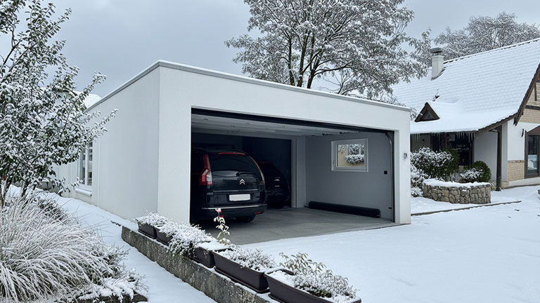 Moderne Großraumgarage aus Beton im Winter mit geöffnetem Tor und zwei geparkten Fahrzeugen