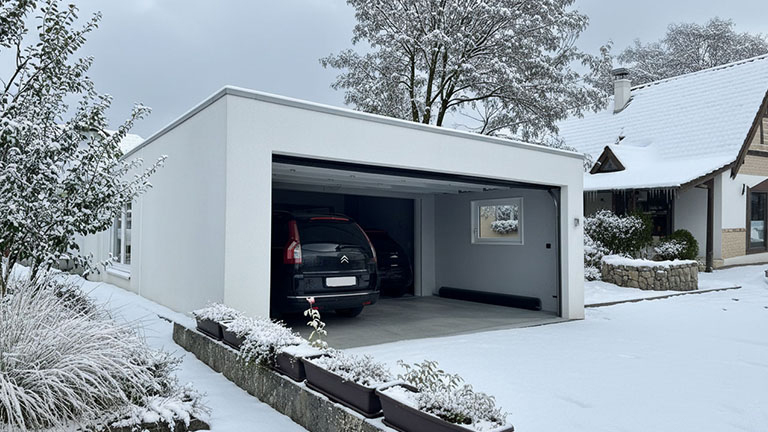 Moderne Großraumgarage aus Beton im Winter mit geöffnetem Tor und zwei geparkten Fahrzeugen