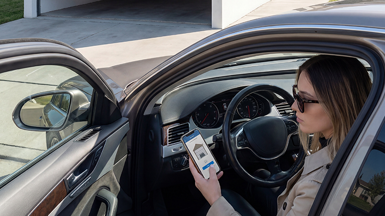 Frau im Auto öffnet per Smartphone-App ein modernes Garagentor – bequem und digital gesteuert