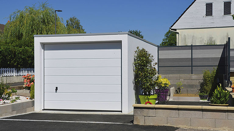 Freistehende weiße Beton-Fertiggarage mit geschlossenem Sektionaltor in moderner Wohnumgebung